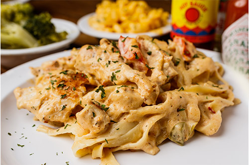 A mouthwatering plate of chicken & shrimp fettuccine, a delectable dish from our authentic soul food menu, featuring tender chicken, succulent shrimp, and creamy fettuccine noodles tossed in a flavorful sauce.