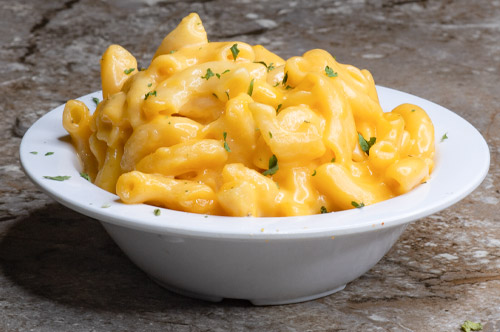 A delightful bowl of mac & cheese, a beloved offering from our authentic soul food menu, featuring perfectly cooked pasta enveloped in a creamy and cheesy sauce.
